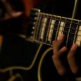 Nahaufnahme einer Hand auf dem Griffbrett einer E-Gitarre im dunklen Licht