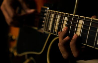 Nahaufnahme einer Hand auf dem Griffbrett einer E-Gitarre im dunklen Licht